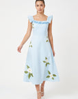 Model wearing Fanm Mon July Dress in light blue with ruffled shoulder straps, white floral embroidery, and a flowing A-line midi skirt