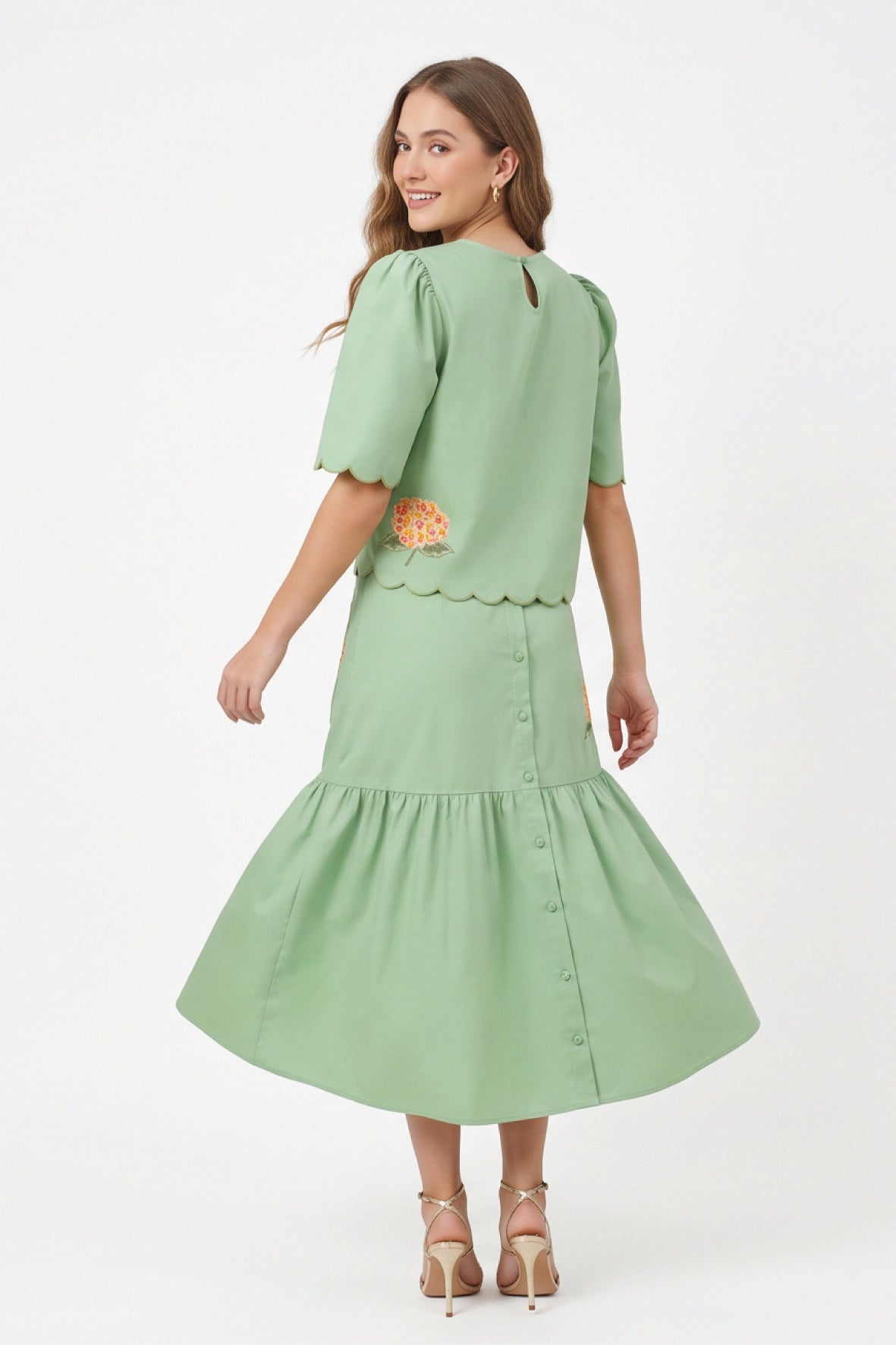 Back view of model wearing Fanm Mon Komarna Set in green showing scalloped detailing along the top, floral embroidery near the back hem, and a gathered midi skirt.
