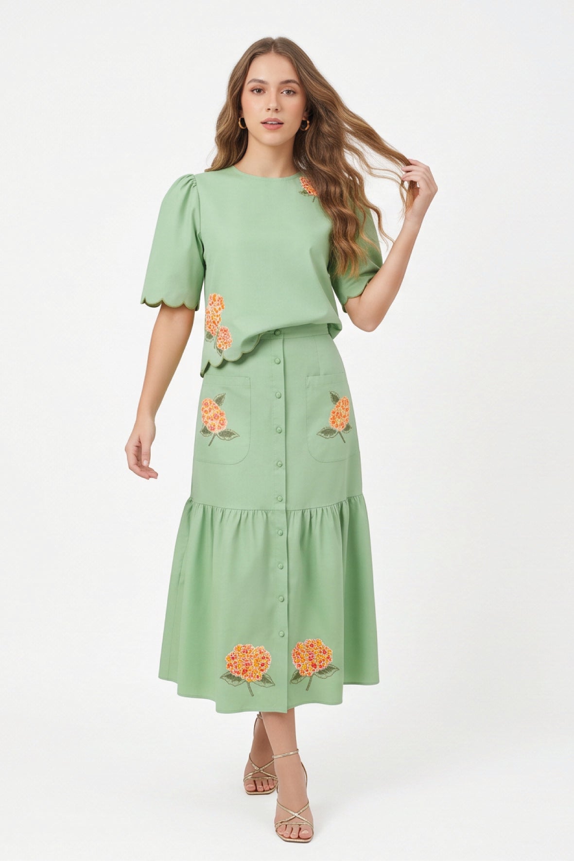 Model wearing Fanm Mon Komarna Set in green tea featuring a puff-sleeve top with scalloped edges, colorful floral embroidery, and a coordinating button-front midi skirt with patch pockets