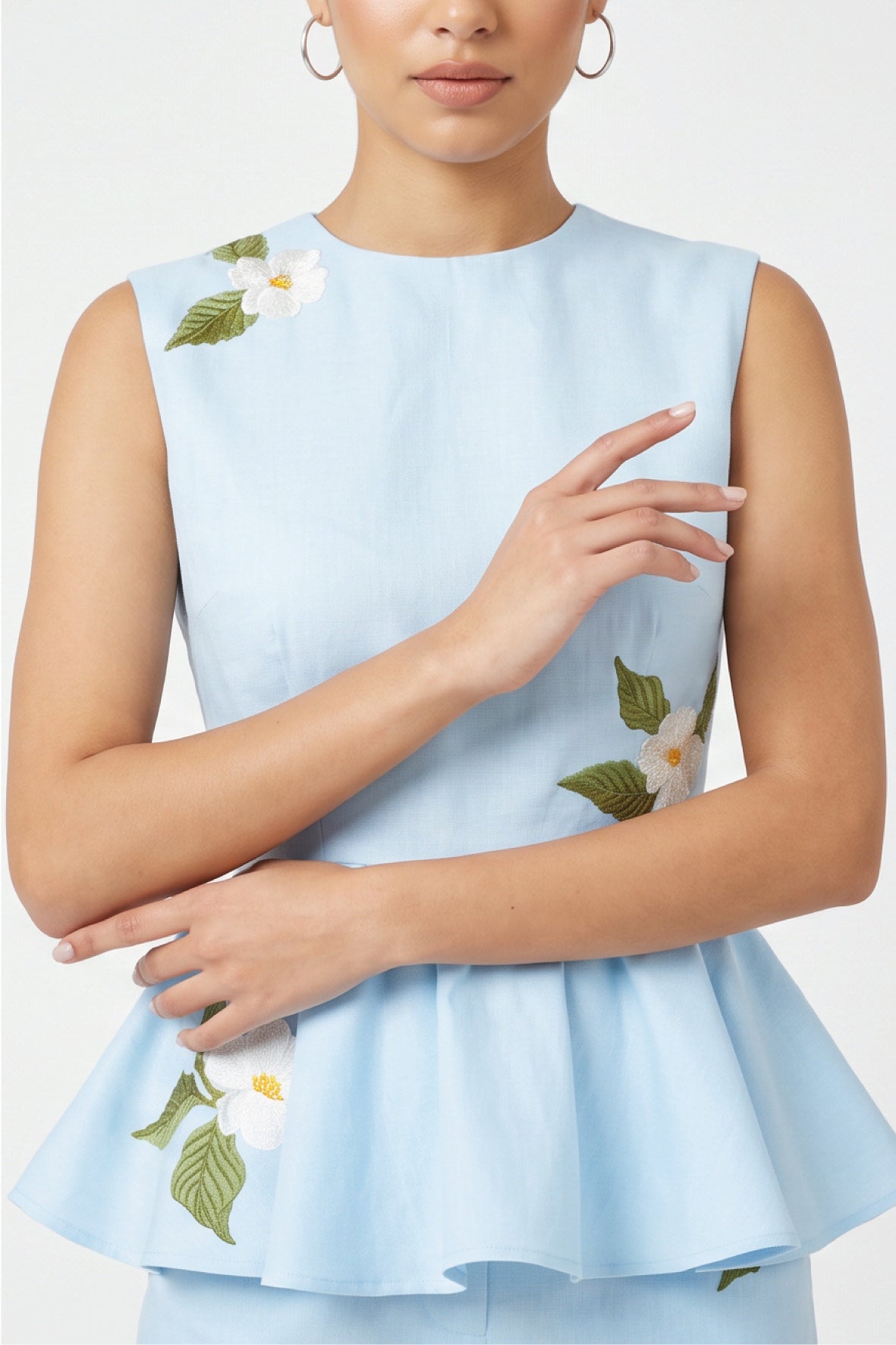 Close-up of Fanm Mon Malez Set in Light Lagoon highlighting the round neckline, tailored sleeveless bodice, gathered peplum, and white floral embroidery with yellow centers and green leaves.