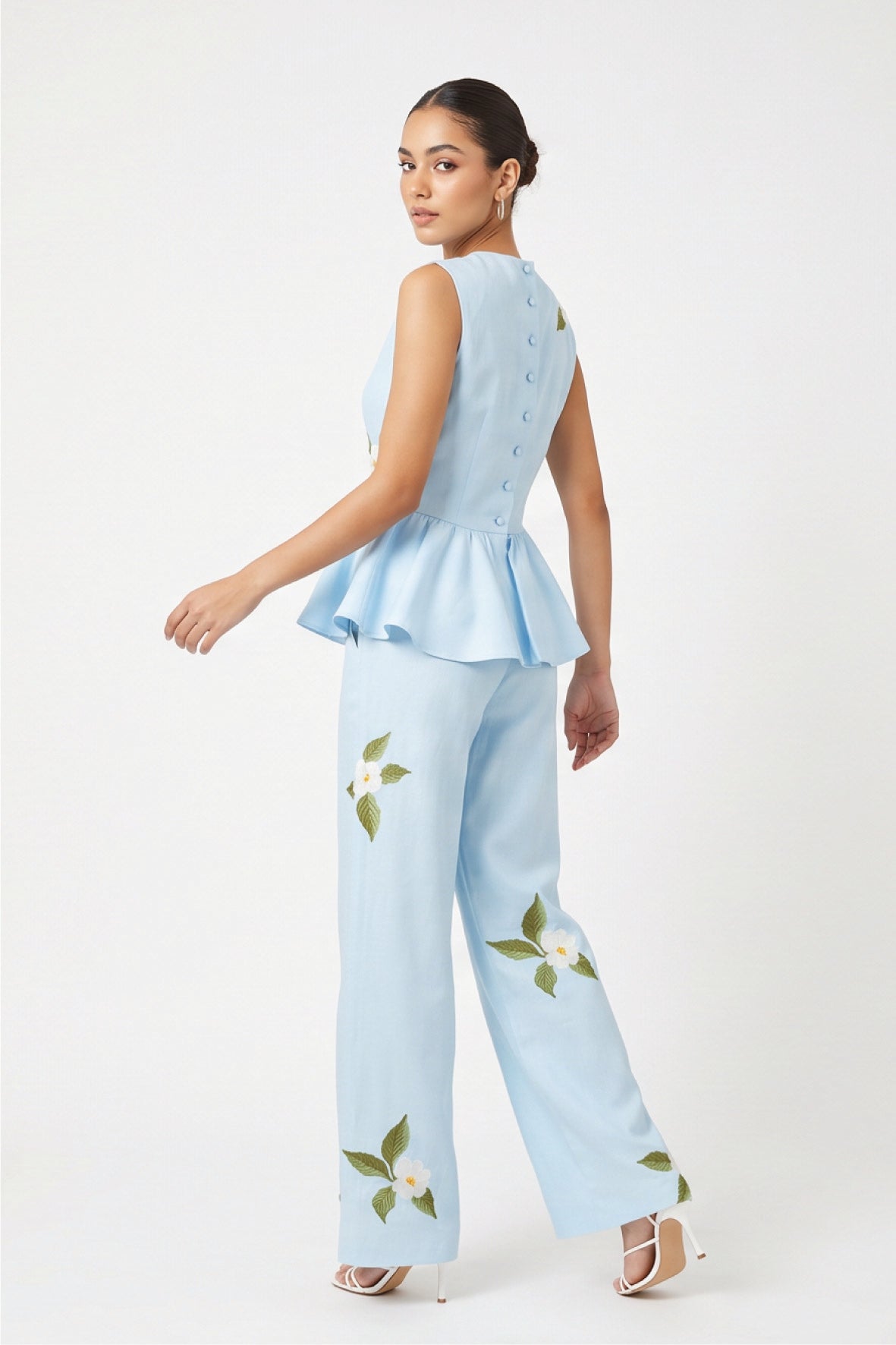 Back view of model wearing Fanm Mon Malez Set in Light Lagoon showing fabric-covered buttons along the fitted peplum top and scattered white floral embroidery on the wide-leg trousers