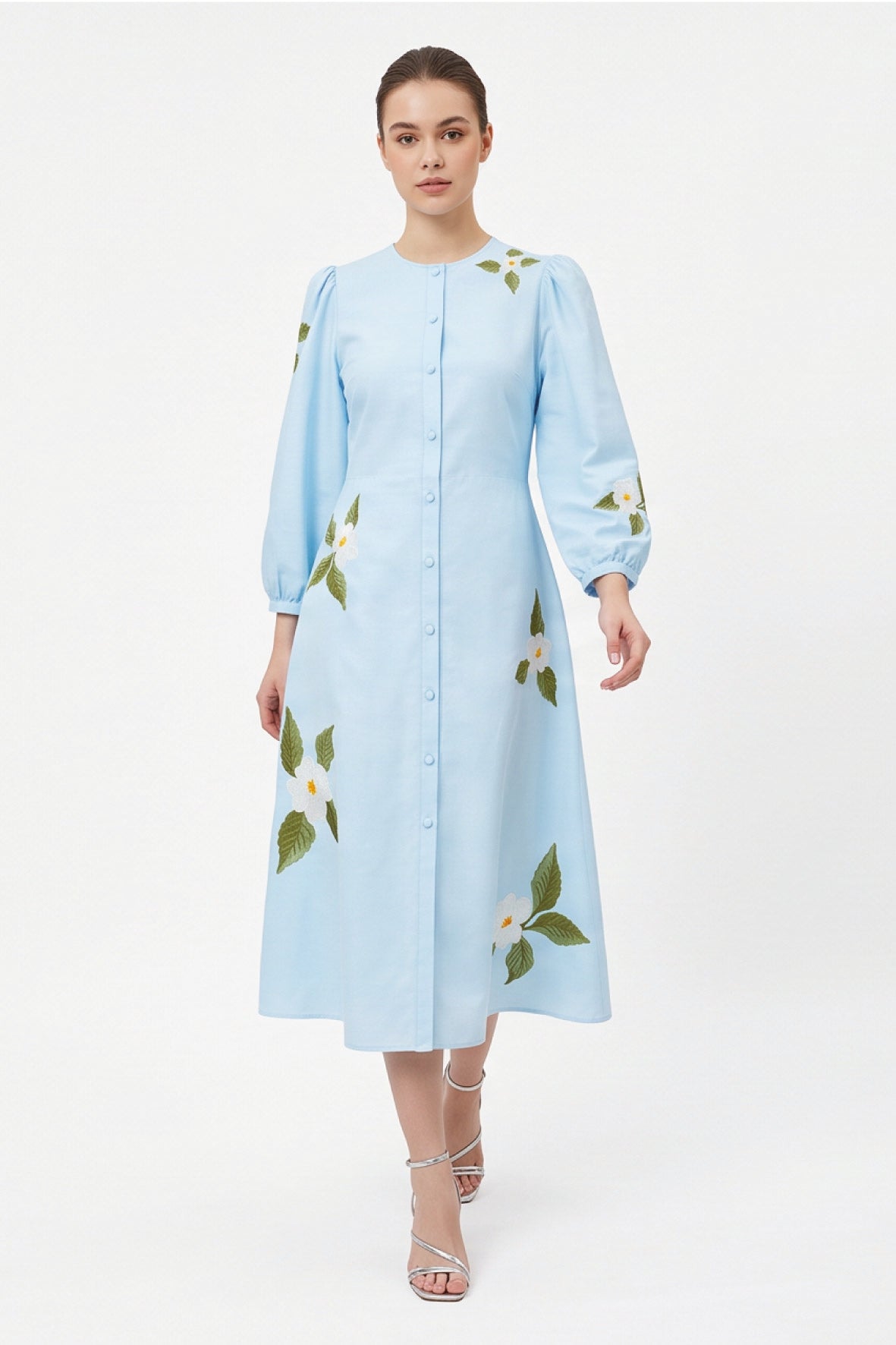 Model wearing the Fanm Mon Paysan Dress in light blue featuring white embroidered blossoms, fabric-covered buttons, and an A-line midi silhouette