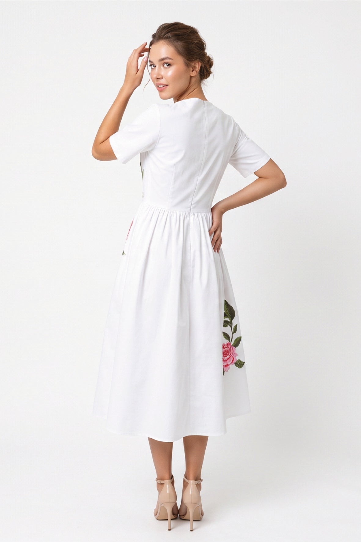 Back view of model wearing Fanm Mon Rumen Dress in white showing the concealed center-back zipper, fitted bodice, gathered waist, and flowing A-line midi skirt with pink floral embroidery along the side.