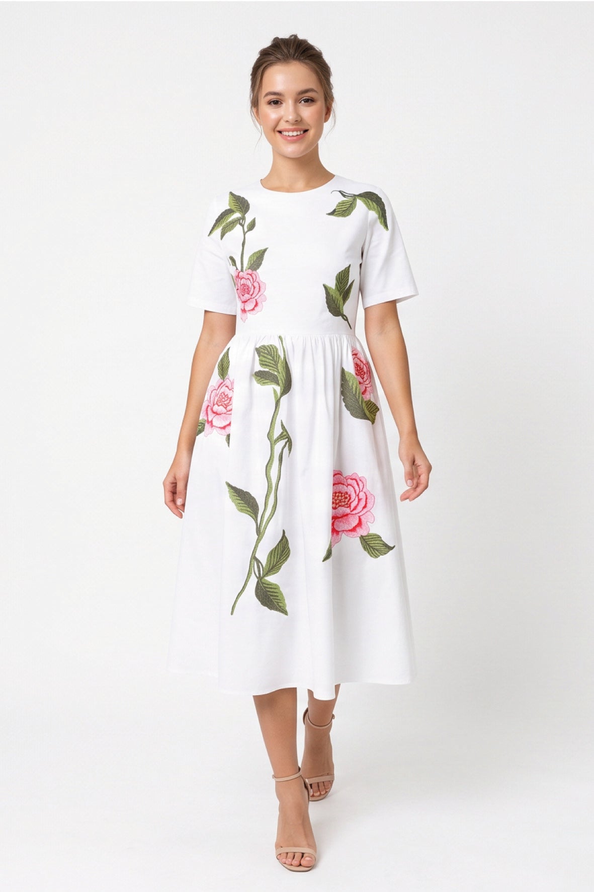 Model wearing Fanm Mon Rumen Dress in white with a round neckline, short sleeves, defined waist, and oversized pink rose embroidery with green foliage across the flowing midi skirt.