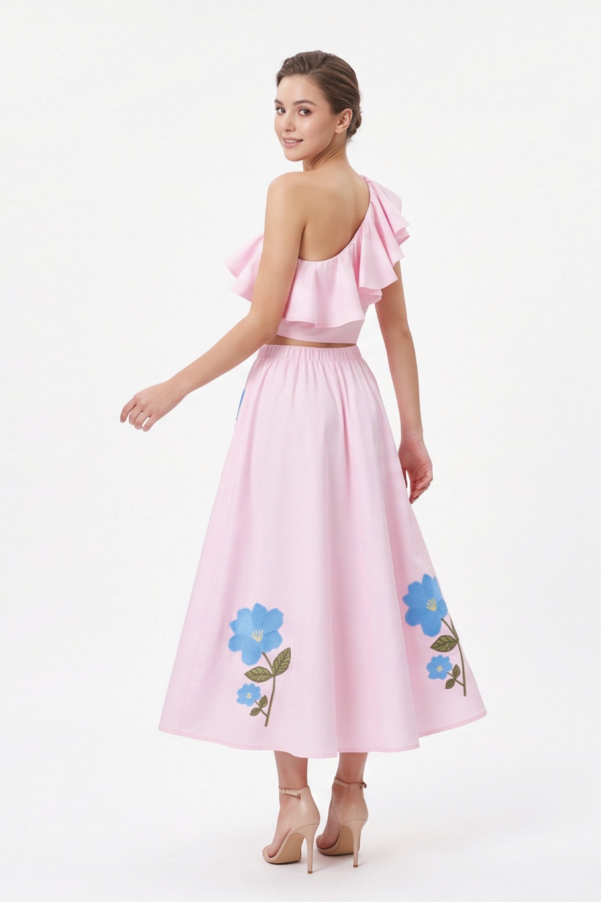Back view of model wearing the Fanm Mon Tamira Set in light pink showing the cascading ruffles on the one-shoulder crop top and floral embroidery along the flowing midi skirt