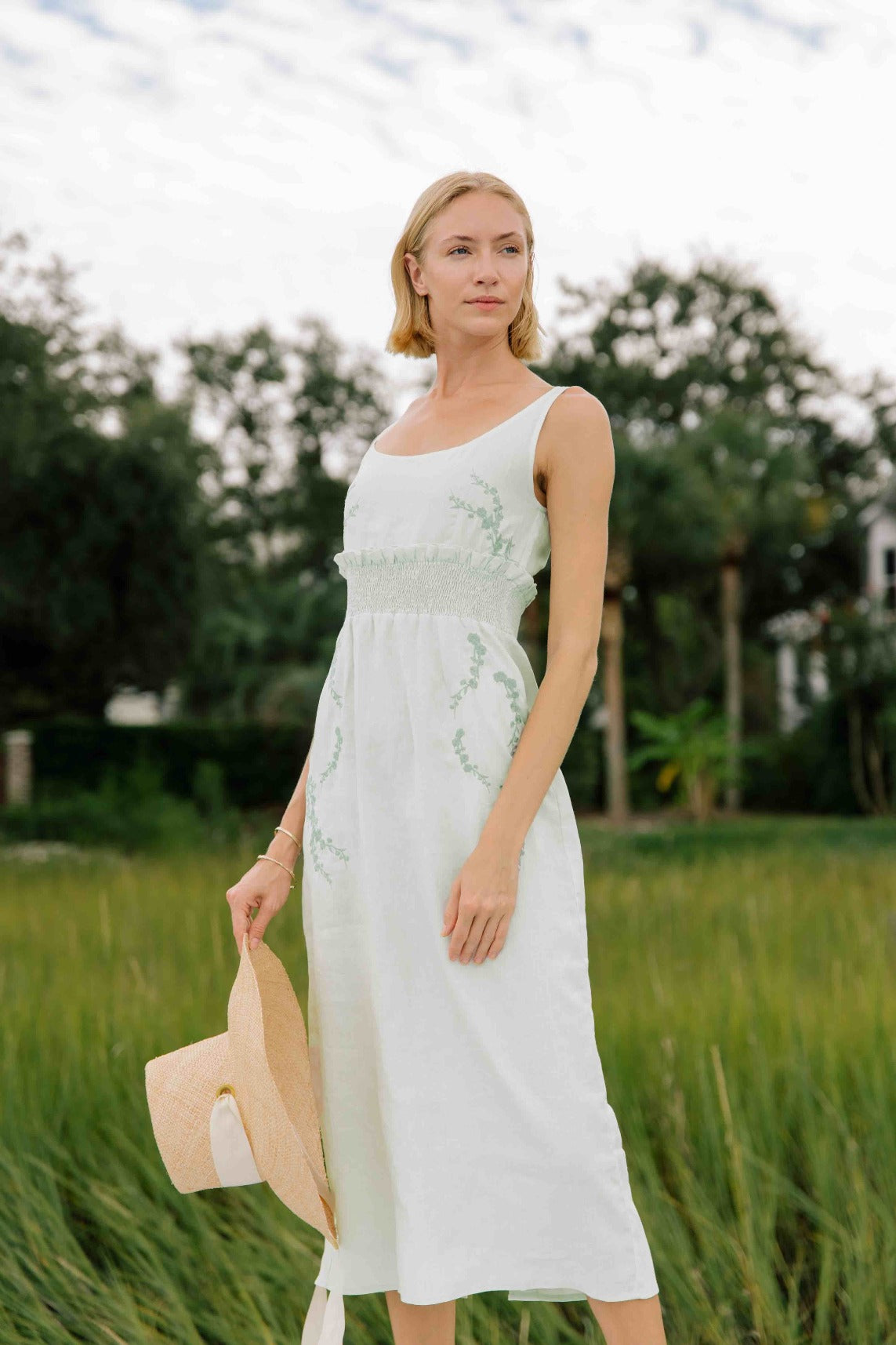 BAHAR Sleeveless Midi Linen Sheath Dress. Featuring a smocked waistband with ruffle trim and a hand-embroidered floral pattern.
