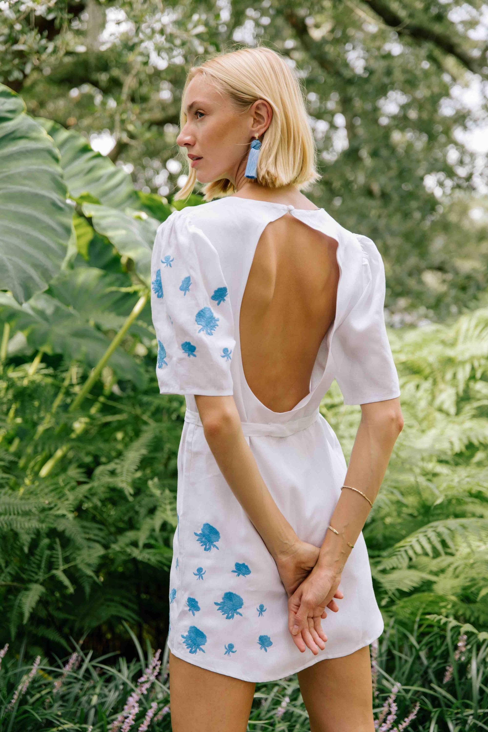 DENIZ Mini Linen Dress. Featuring a peephole open back and button closure. Round neck, with belted detail at the waist and on sleeves with front embroidery pattern.