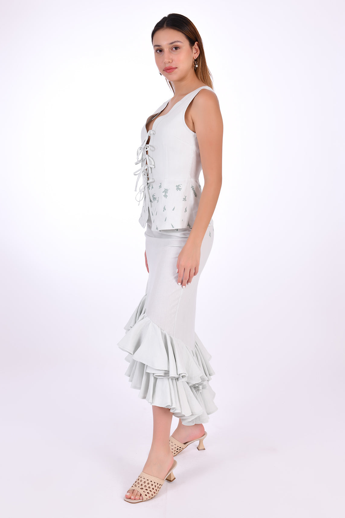 Fanm Mon Flamen Skirt Set, side view. 2 Piece Linen Top and Skirt Set includes a sleeveless top with a v-neck, a tie-up front, and a peplum flare bottom with delicate embroidery. The midi-length linen skirt is complemented by a gathered front detail and coordinating embroidery.