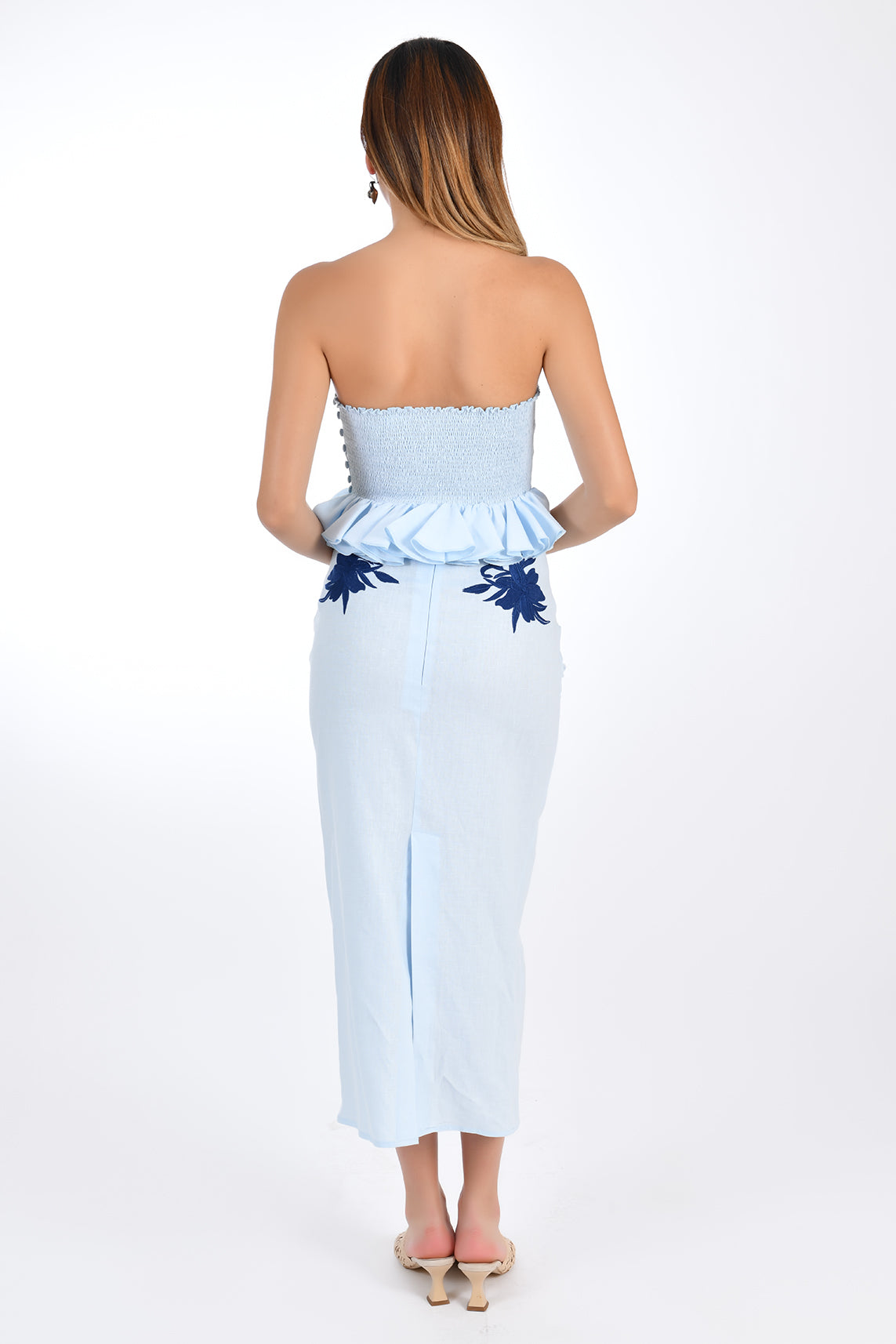 Fanm Mon Arina 2 Piece Linen Skirt Set. Back view of strapless ruffle peplum top and straight midi length skirt with back embroidery detail and back slit and zipper closure.